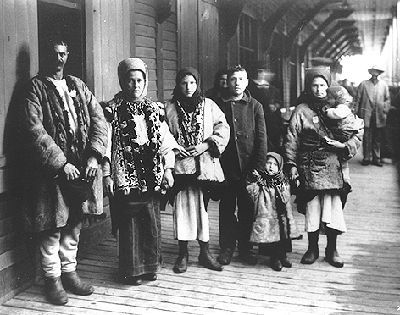 Black and white photo of a family of Ukranian immigrants wearing traditional garb. From left to right: the father, mother and five children. They are at a station.