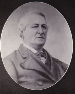 Black and white photo of a man, shoulders to the side, looking straight ahead. He wears a jacket, shirt with a white collar and a bow tie.