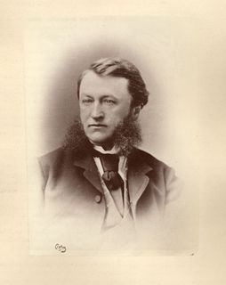 Portrait photo of Toussaint-Antoine-Rodolphe Laflamme wearing a black jacket and large tie under which may be seen a diamond motif sweater and a white shirt. He is looking to the photographer's right.