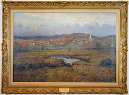 Framed painting of the church and homes of the village of Arthabaska near the top of the canvas with the sky overhead. Below the village, a field crossed by a river. The yellow, orange and green tones are indicative of the onset of fall. The gold-coloured frame features ribbon molding trim.