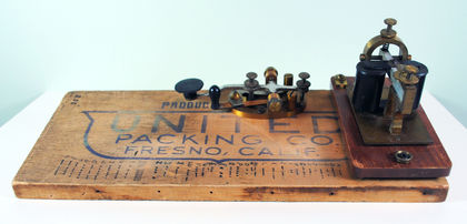 Telegraph transmitter consisting of a wooden board inscribed with United Packing Co. Fresno, Calif. and a key to tap out and receive messages in Morse Code.
