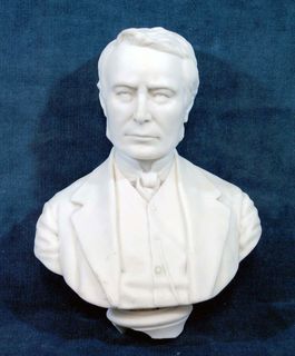 White bust of Mr. Blake's head and shoulders. He is wearing a jacket and a bow tie.