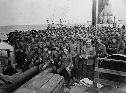 Group of soldiers on the deck of a ship looking towards the camera. They are all wearing military attire.